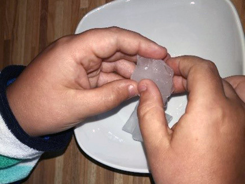 Ein Kind hält einen Eiswürfel in den Händen.