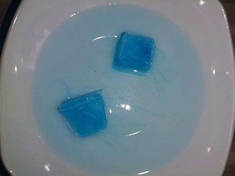 Eingefärbte Eiswürfel schmelzen in einem Teller.